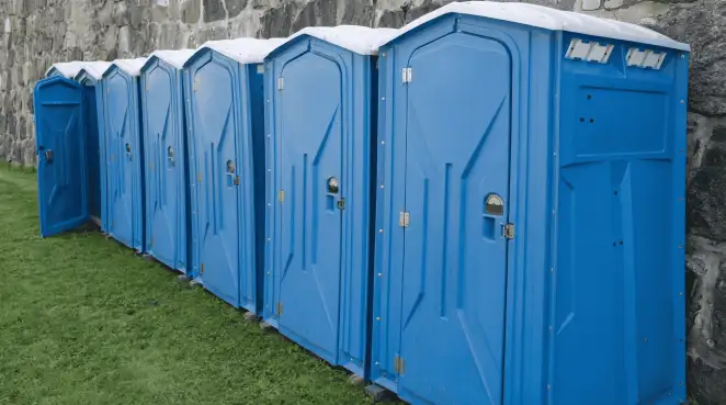 Row of blue portable toilets lined up on grass against a stone wall for event sanitation in Pasadena, CA