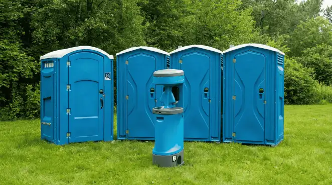 Four blue portable toilets and a matching hand washing station on grass near trees, a common sight at local outdoor events in Pasadena, CA