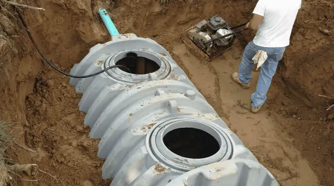 Septic tank installation showing a technician compacting soil around a new poly septic tank in an excavation pit in Pasadena, CA